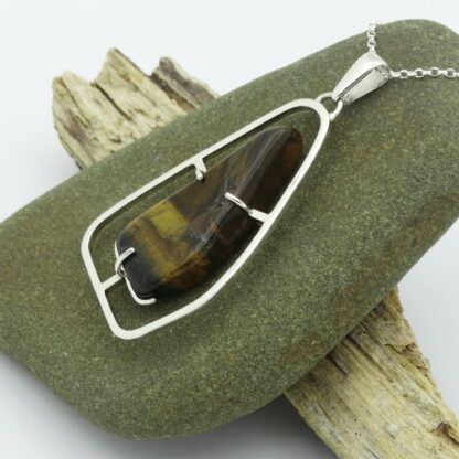 Tiger's eye silver pendant presented on a pebble