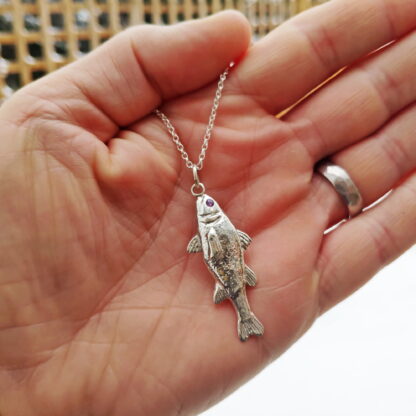 Silver fish pendant with natural amethyst eye in hand