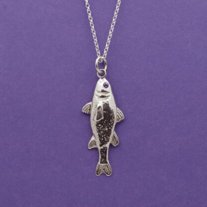 Silver fish pendant with natural amethyst eye set against a purple background