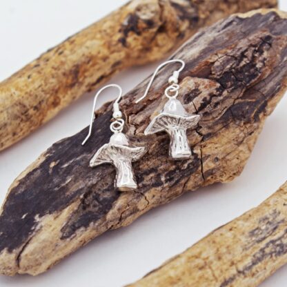 Silver mushroom earrings presented on a log