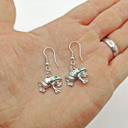 Silver frog earrings presented in the palm of a hand